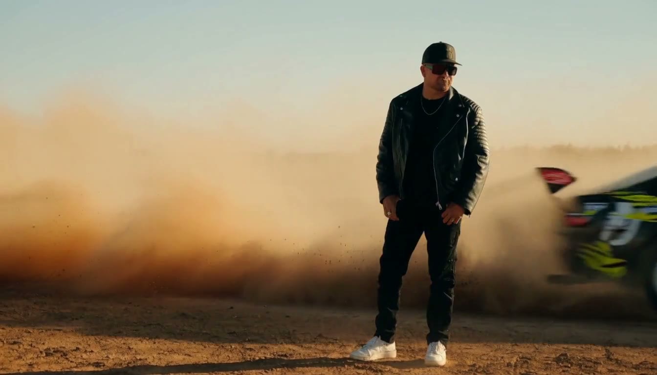 MiniMax H3 AI video example showing a man in a leather jacket stands confidently as a vintage car performs a dramatic drift in the background