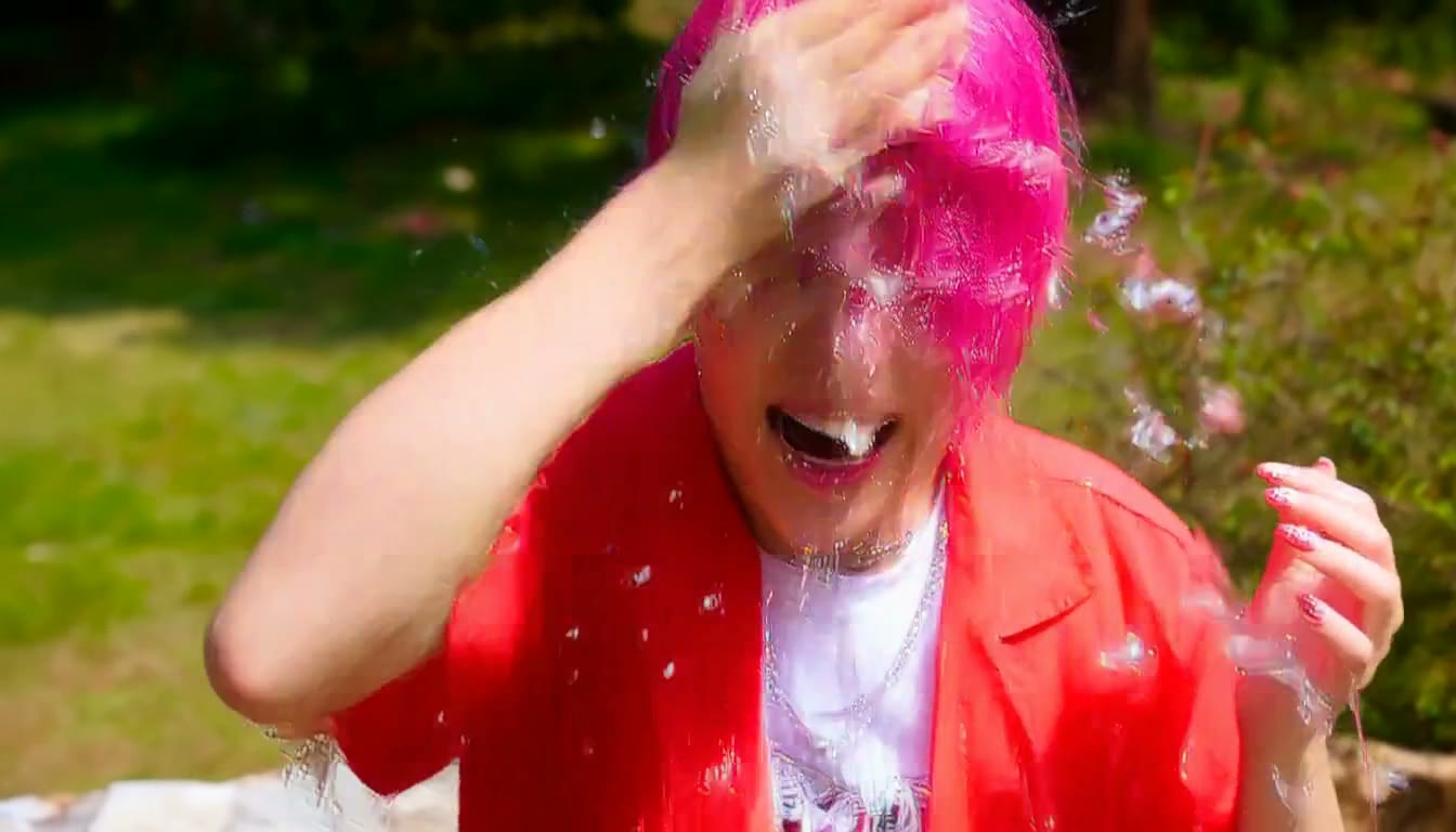 MiniMax H3 AI video example showing a person with pink hair and a red jacket is playfully splashing water on their face in a sunny outdoor setting
